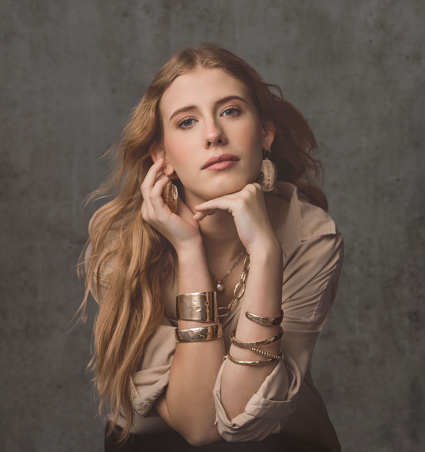 Model wearing layered bronze bangles and jewelry in a dark studio setting