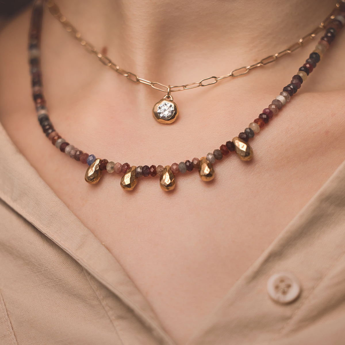 Close-up of Spinel Teardrops Necklace showcasing colorful faceted spinel beads and five golden bronze teardrop charms on a beige shirt